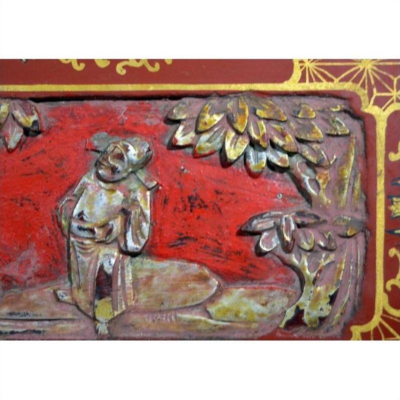 Red lacquer wood box with gilt gold floral inlay and carved wood details beneath trees, on plain background.