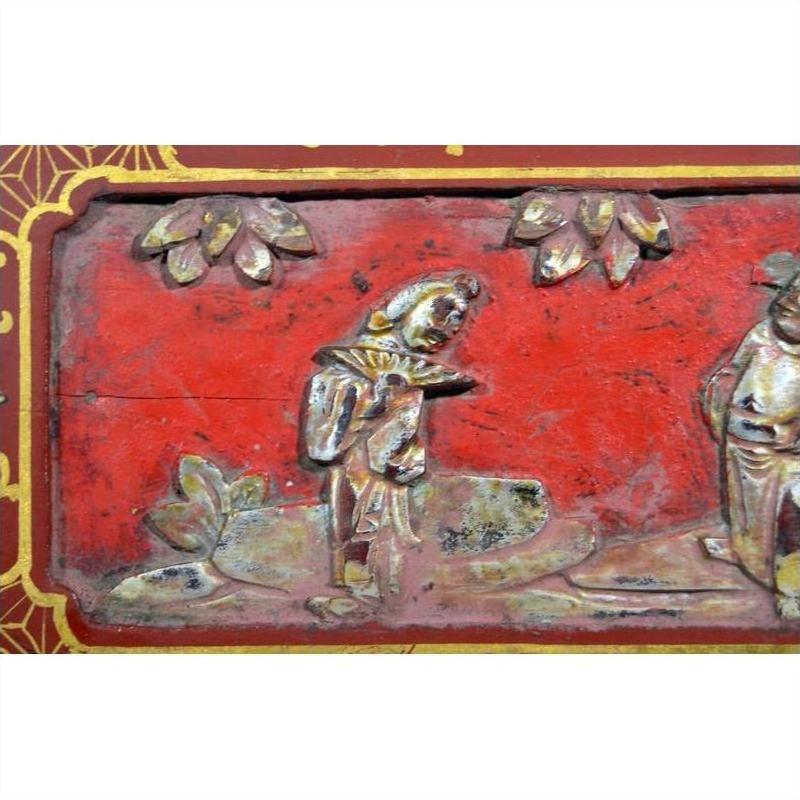 Red and gold lacquer box with floral inlay and a figure near plants, shown against a plain background.