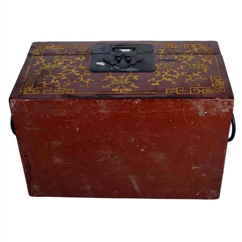 Red and gold lacquered Chinese box with raised scene on lid, metal latch, antique style, shown from front angle.