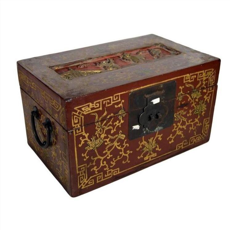 Red and gold Chinese lacquer box with raised top scene, metal handles, and ornate front lock, close-up view.