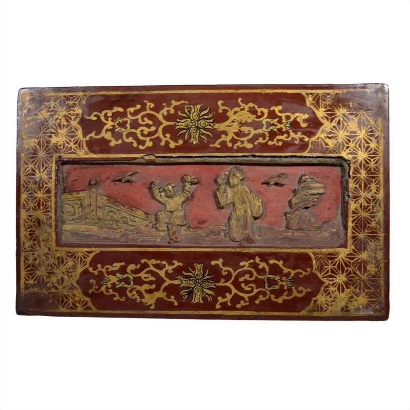 Red and gold lacquered Chinese antique box with raised relief scene of people and birds, close-up view.