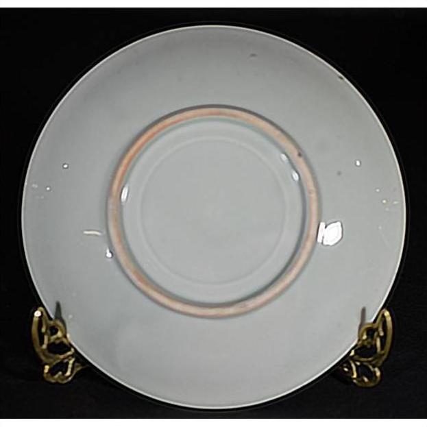 White porcelain plate with gold rim, hand painted and embossed, on a brass stand against a black background.