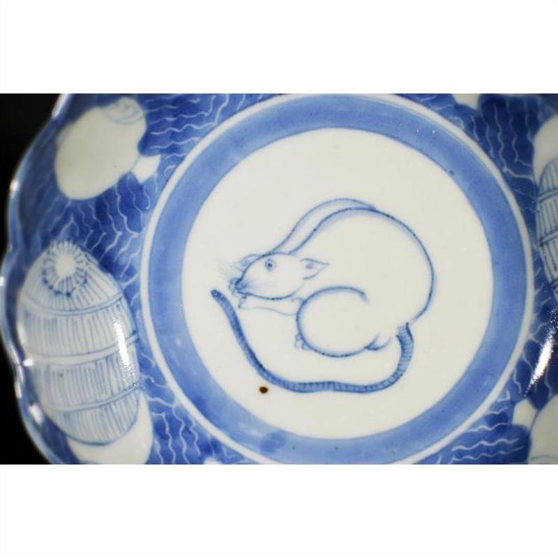 White ceramic scalloped dish with central crouching mouse and barrel cartouche, ornate decorative borders, close-up.