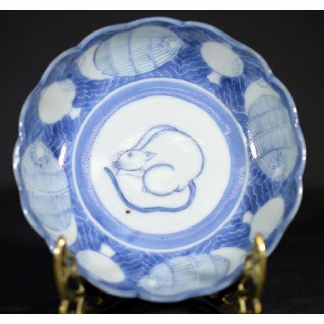 Blue and white ceramic scalloped dish with crouching mouse and barrel design, displayed on a stand.