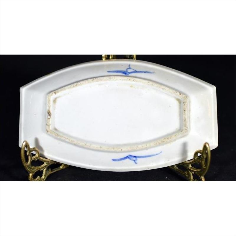 Blue and white ceramic boat-shaped dish with misty landscape and two birds, ornate brass stand, close-up.