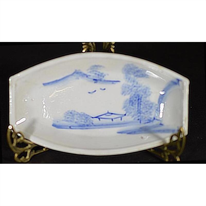 Close-up of antique brass boat-shaped dish with misty landscape and two flying birds, displayed on ornate stand.