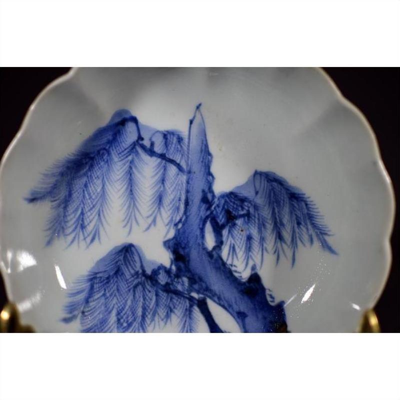 White porcelain fluted plate with scalloped edge, featuring detailed wind-swept pine design, close-up view.