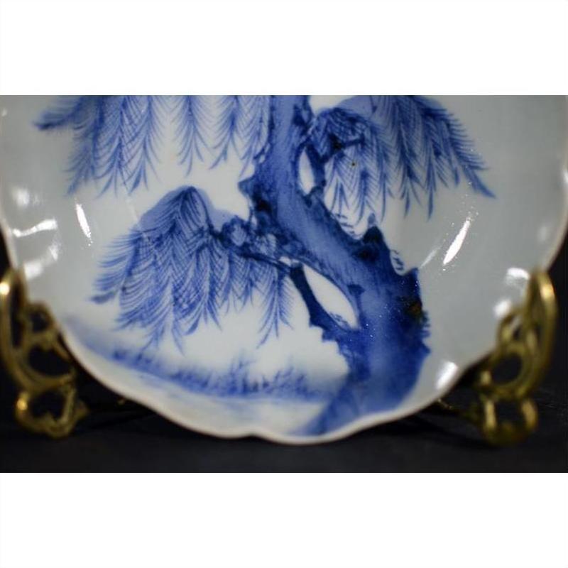 White porcelain fluted plate with Wind-Swept Pine design on decorative brass stand, close-up.
