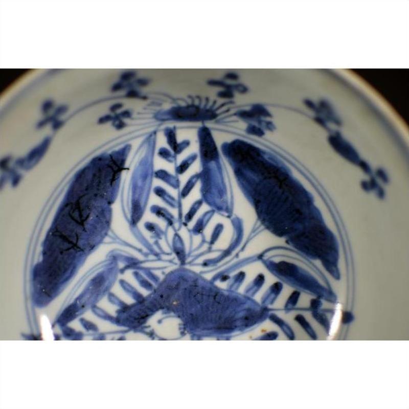 Close-up of antique Asian porcelain dish with foliate hill motif, rustic brushwork, and a small surface crack.