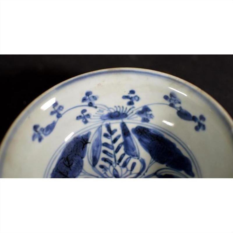 Close-up of a white porcelain Asian dish with foliate hill motif and rustic brushwork on a dark background.
