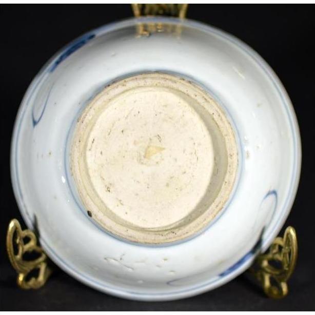 White porcelain dish with foliate hill motif, bottom view, displayed on ornate brass stand.