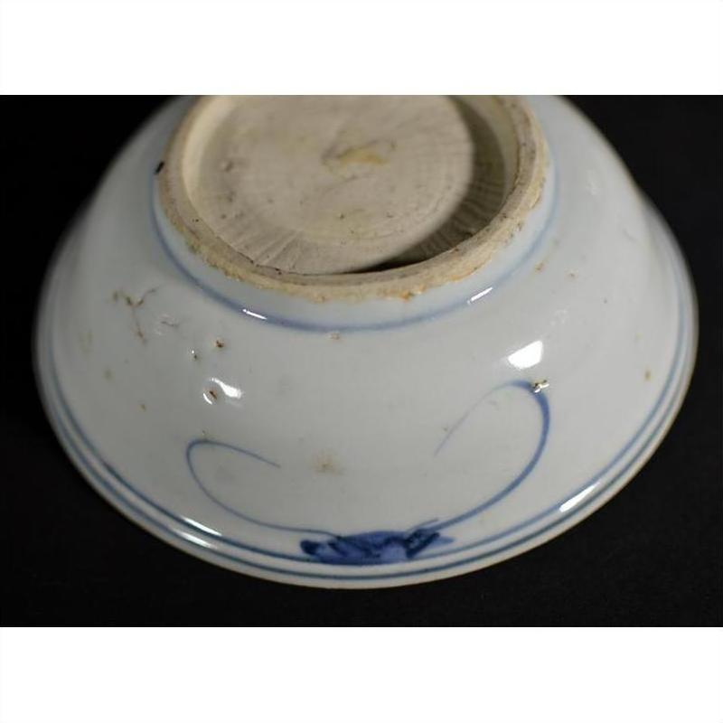 Close-up of blue and white porcelain dish base with foliate motif and rustic unglazed textured bottom.