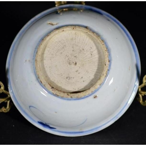 Close-up of the underside of a blue porcelain Asian dish with botanical spray pattern, rough base, on black background.