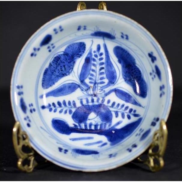 Blue porcelain dish with radial botanical design, displayed on a gold stand against a dark background, close-up.