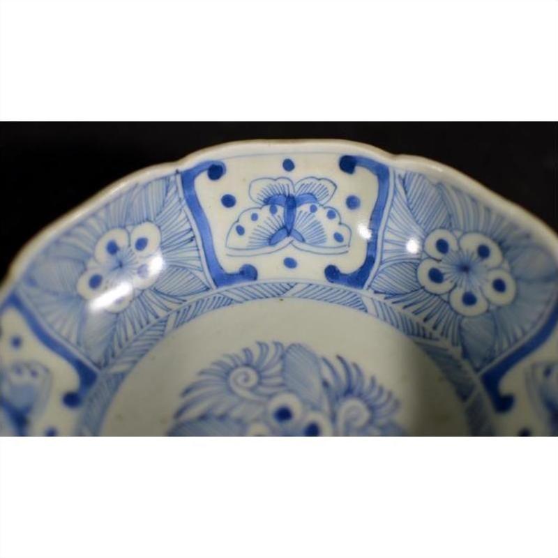 Close-up of blue and white porcelain Chinese bowl with butterfly cartouches, petal rim, floral and geometric patterns.