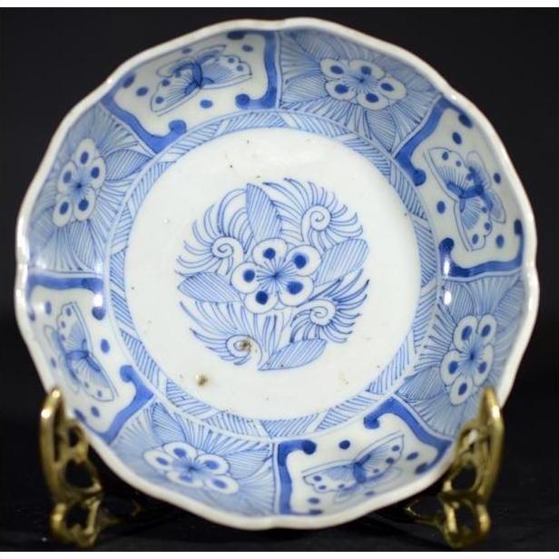 White porcelain bowl with butterfly cartouches and petal rim, on ornate brass stand against a dark background.
