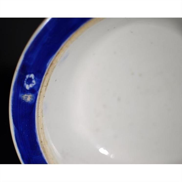 Close-up of antique Asian plate with broad blue rim, minimal white center, small mark visible on rim edge.