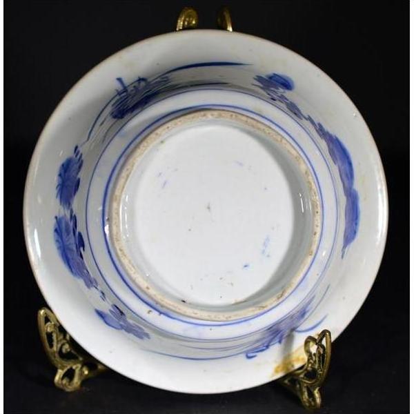 Close-up of an antique Asian deep plate with a broad blue rim, minimal center, on a gold stand against a dark background.