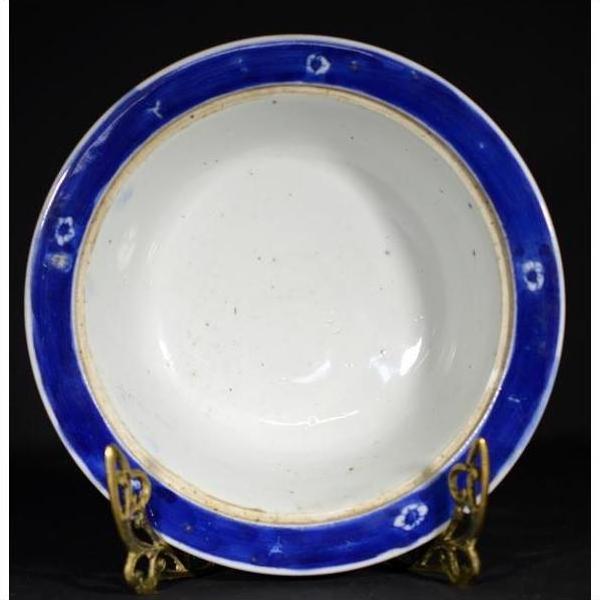 Blue-rimmed antique Asian deep plate on gold stand, black background, ceramic tableware close-up.