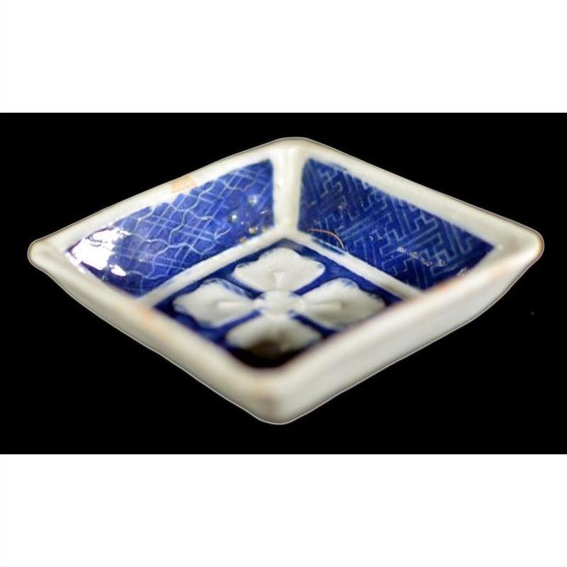 Close-up of an antique blue and white ceramic bowl with raised petal pattern, grid-textured sides, and floral center.