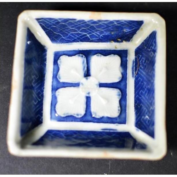 Close-up of antique blue and white ceramic bowl with raised petal center pattern and grid textured sides.