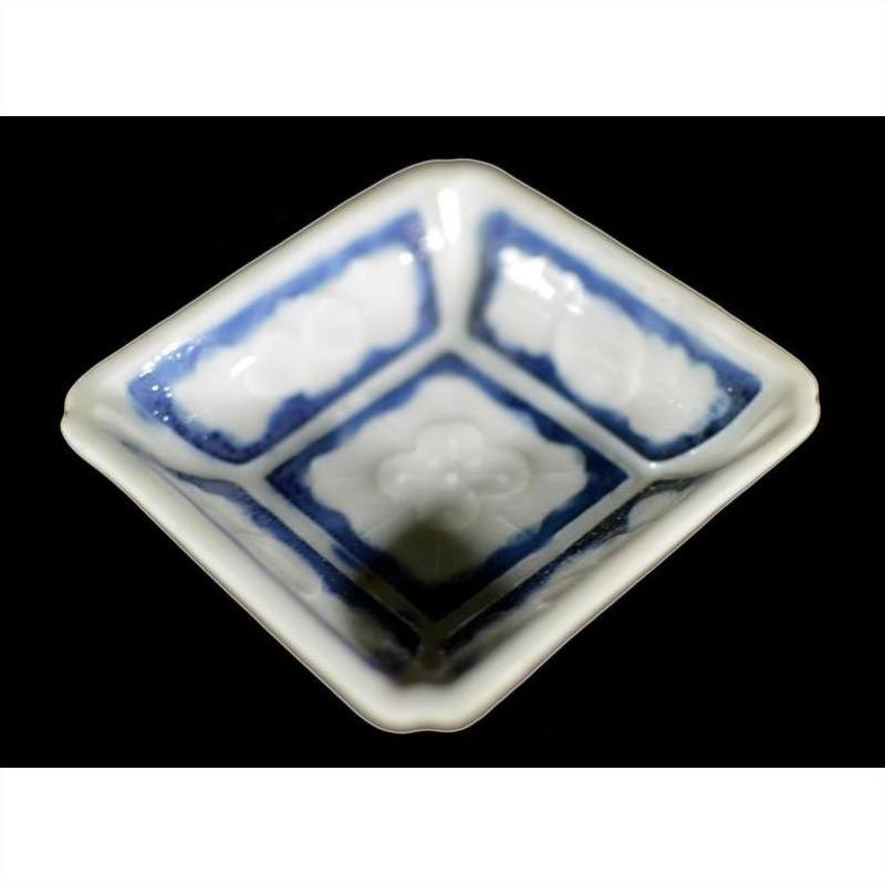 Close-up of antique blue ceramic bowl with embossed blossom detail, blue-washed corners, set on black surface.