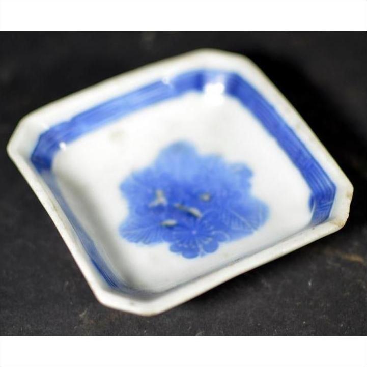 Close-up of blue and white ceramic dish with chrysanthemum bloom and geometric frame, on a dark surface.