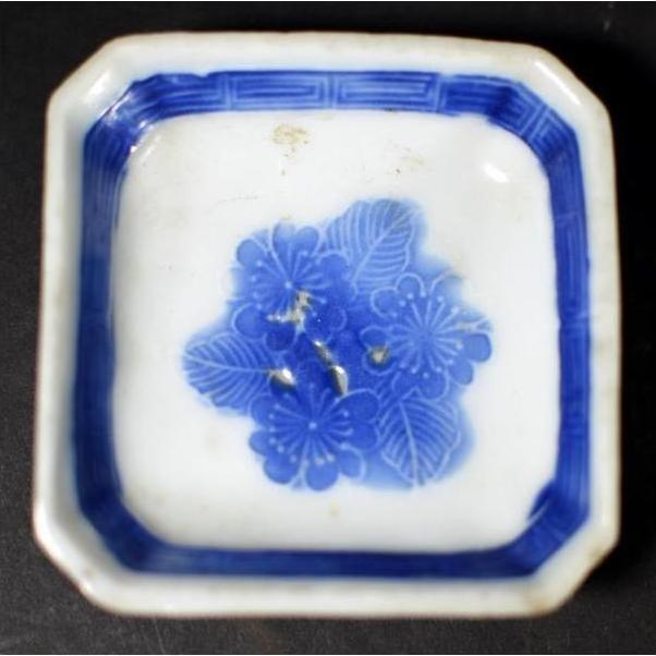 Close-up of antique blue and white ceramic dish with chrysanthemum center and blue geometric frame pattern.