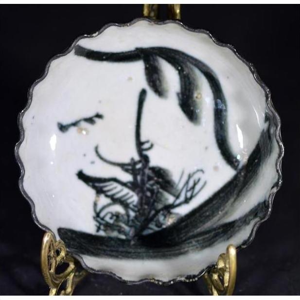 White porcelain plate with ink-style bamboo design on decorative gold stand, close-up.