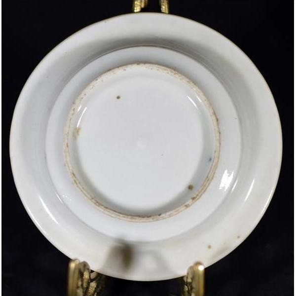 Close-up of the underside of a small antique porcelain dish with blue dashes, landscape sketch, slight rim wear, on brass stand.