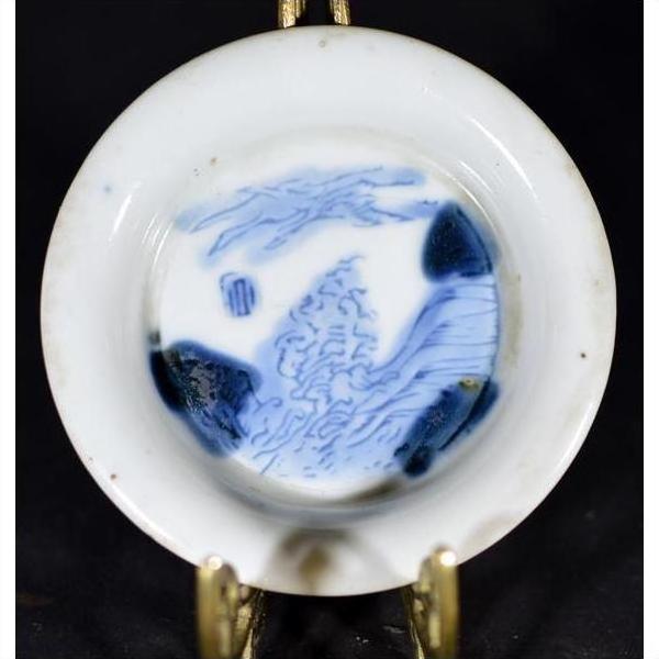 Blue and white porcelain dish with landscape sketch and blue dashes, displayed on decorative metal stand.