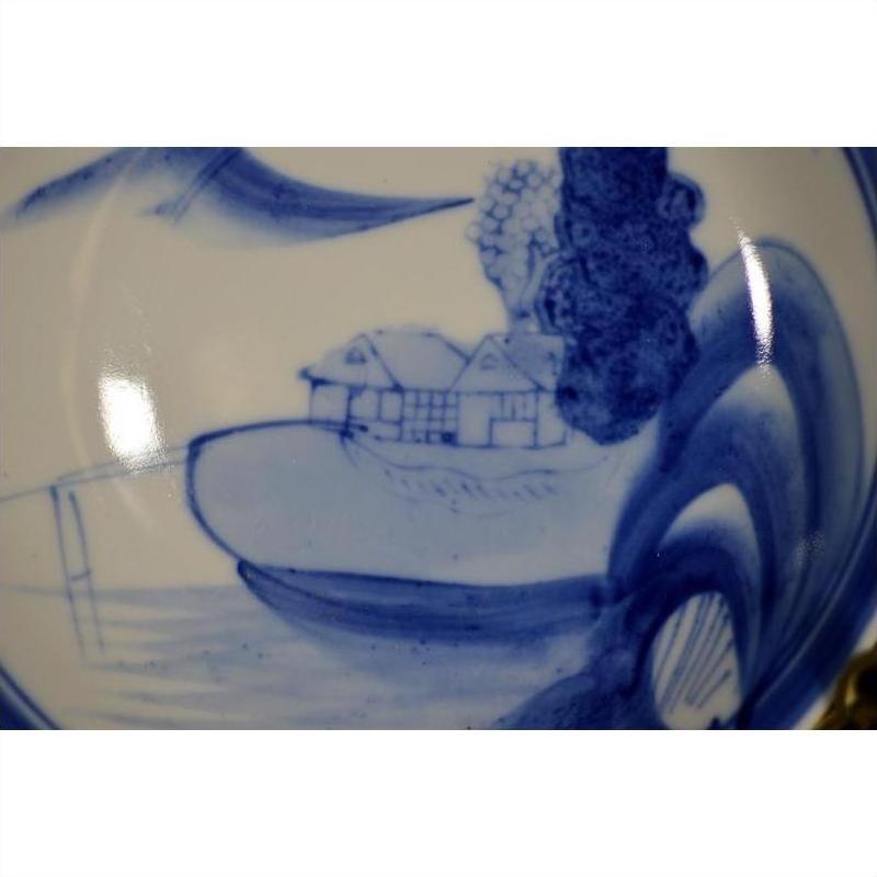 Blue and white porcelain plate with hand painted seated scholar by a river, antique Chinese style, close-up.