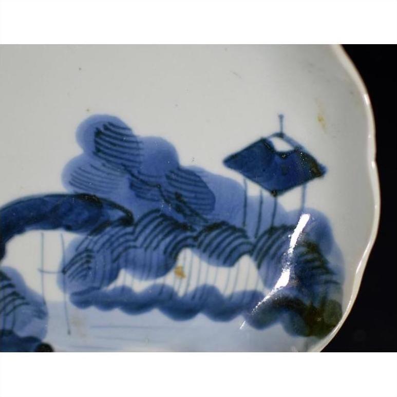 White porcelain plate with painted blue clouded mountain landscape, trees, and a tranquil sloped-roof structure.