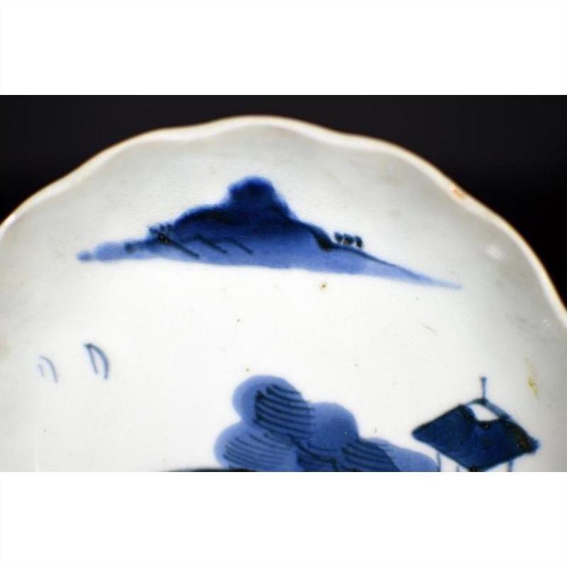 Close-up of white porcelain plate with hand-painted Chinese clouded mountain landscape and trees along rim.