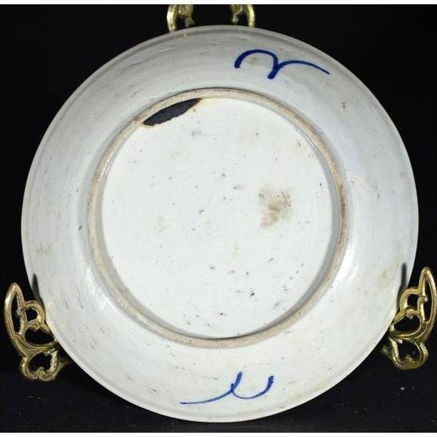 Close-up of blue and white porcelain underside with hand-painted marks, chips, and discoloration visible.