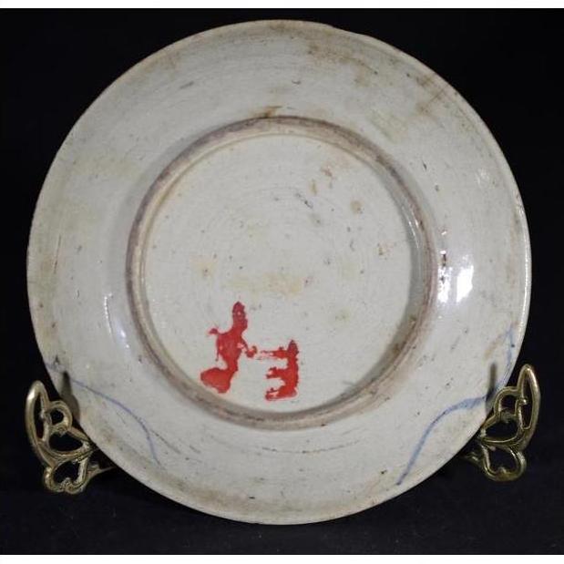 Close-up of an antique hand-painted porcelain plate with butterfly design on a metal stand, black background.