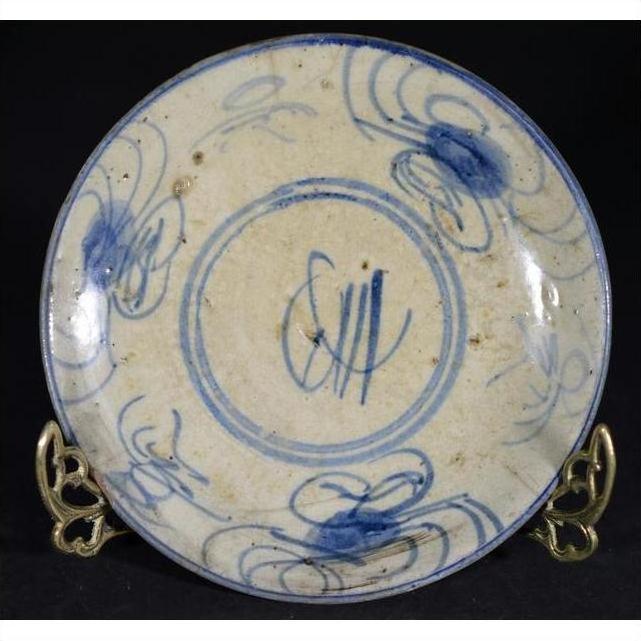 Close-up of blue and cream antique Chinese hand-painted porcelain plate with butterfly, on metal stand, dark background.