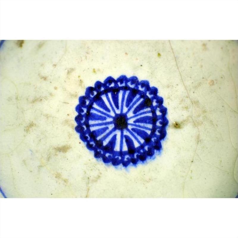 Close-up of a blue floral pattern on a white textured ceramic plate with radial medallion sunburst design.