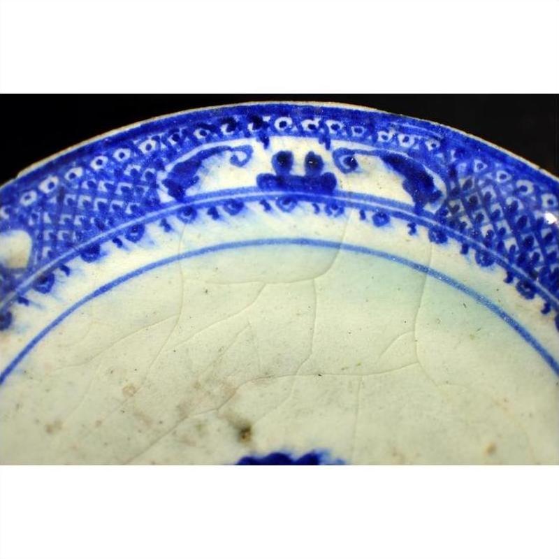 Close-up of blue and white ceramic plate with radial medallion design, blue loop border, and crackled glaze.