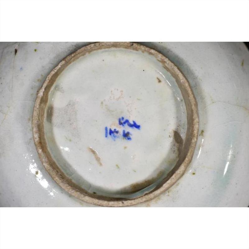 White ceramic plate underside close-up with blue handwritten markings near the center, indoors.