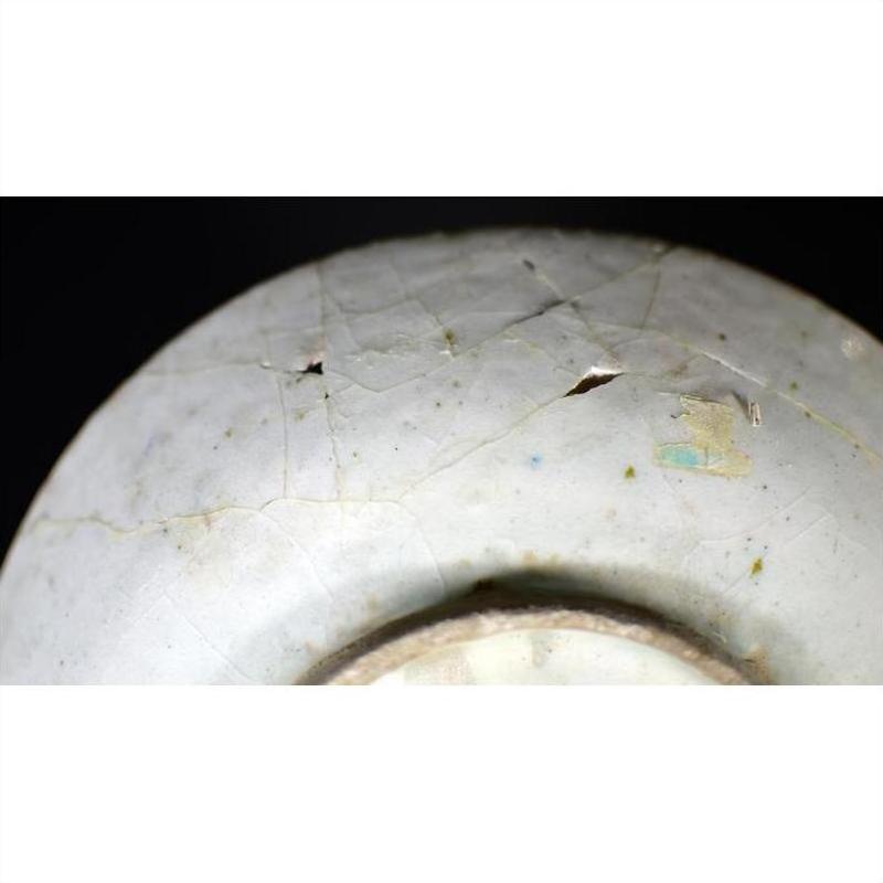 Close-up of a white ceramic plate with radial medallion pattern, showing cracks, chips, and holes.