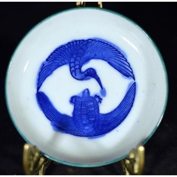 Metal circular dish with antique crane and turtle design, displayed on a metal stand, symbolic embrace motif.