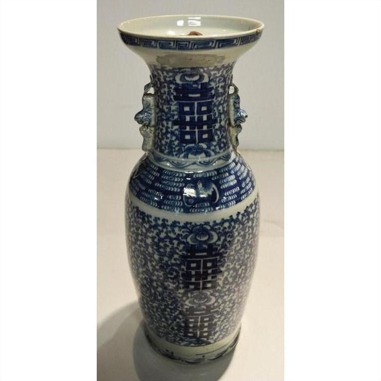 Close-up of blue and white ceramic Chinese vase with floral patterns, decorative handles, and weathered finish.