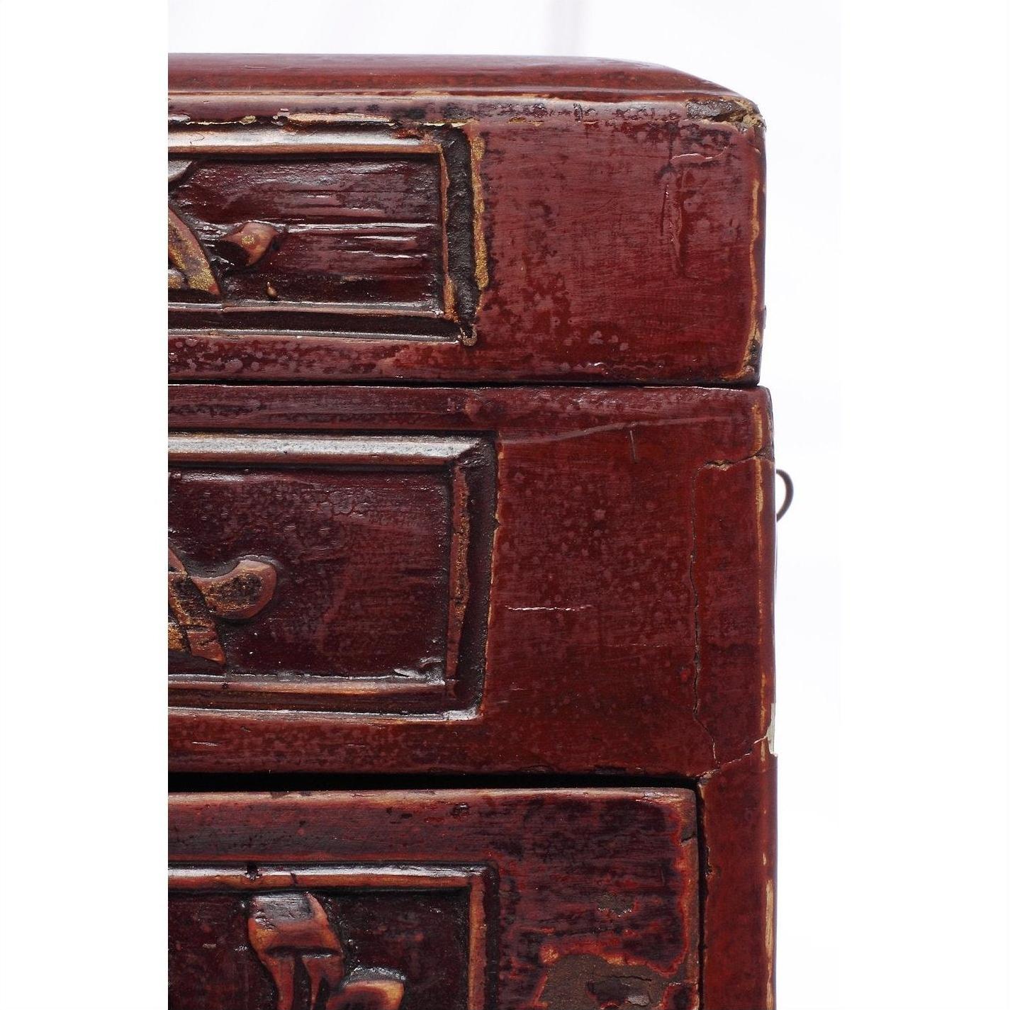 Close-up of dark red lacquer antique Chinese jewelry box with worn edges and carved drawers.