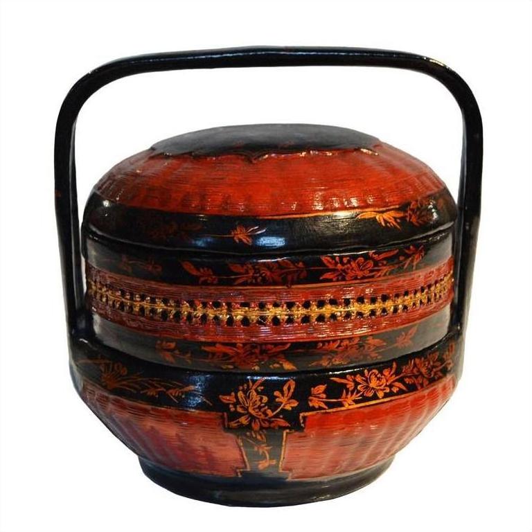 Red and black lacquered Chinese lunch box with handle, floral designs, and intricate patterns, close-up view.