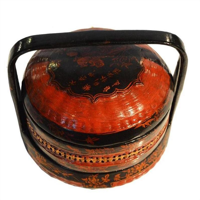 Close-up of round red and black lacquered Chinese lunch box, tiered design with handle and gold floral accents.