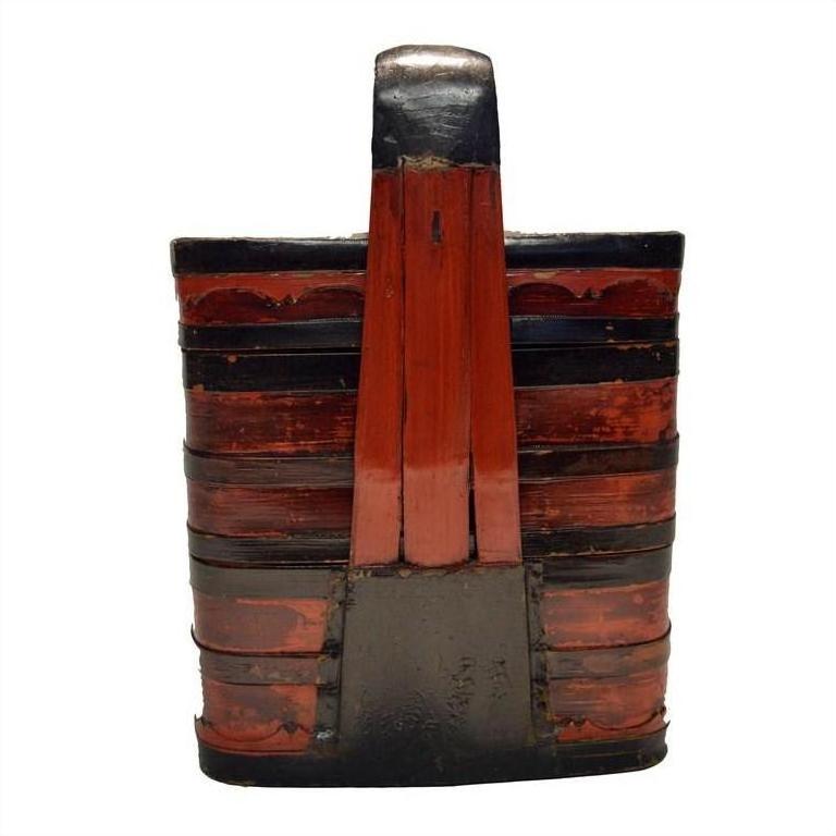 Close-up of red and black lacquered Chinese wooden tiered food basket with hand-painted slats and tall single handle.