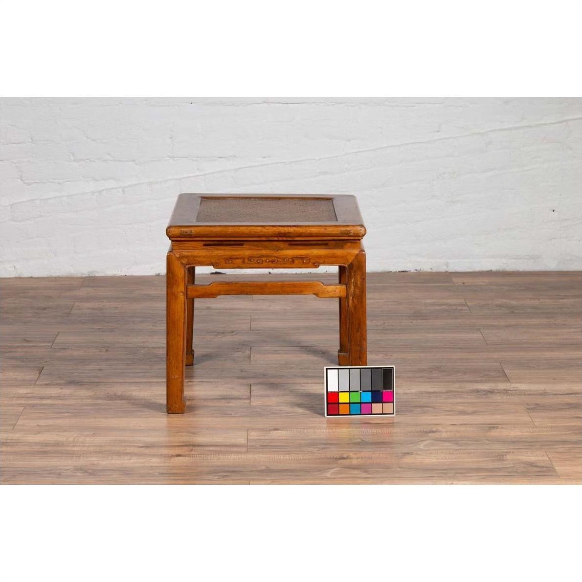 Brown elmwood Ming style waisted side table with horsehoof legs on wooden floor, color calibration card in front.