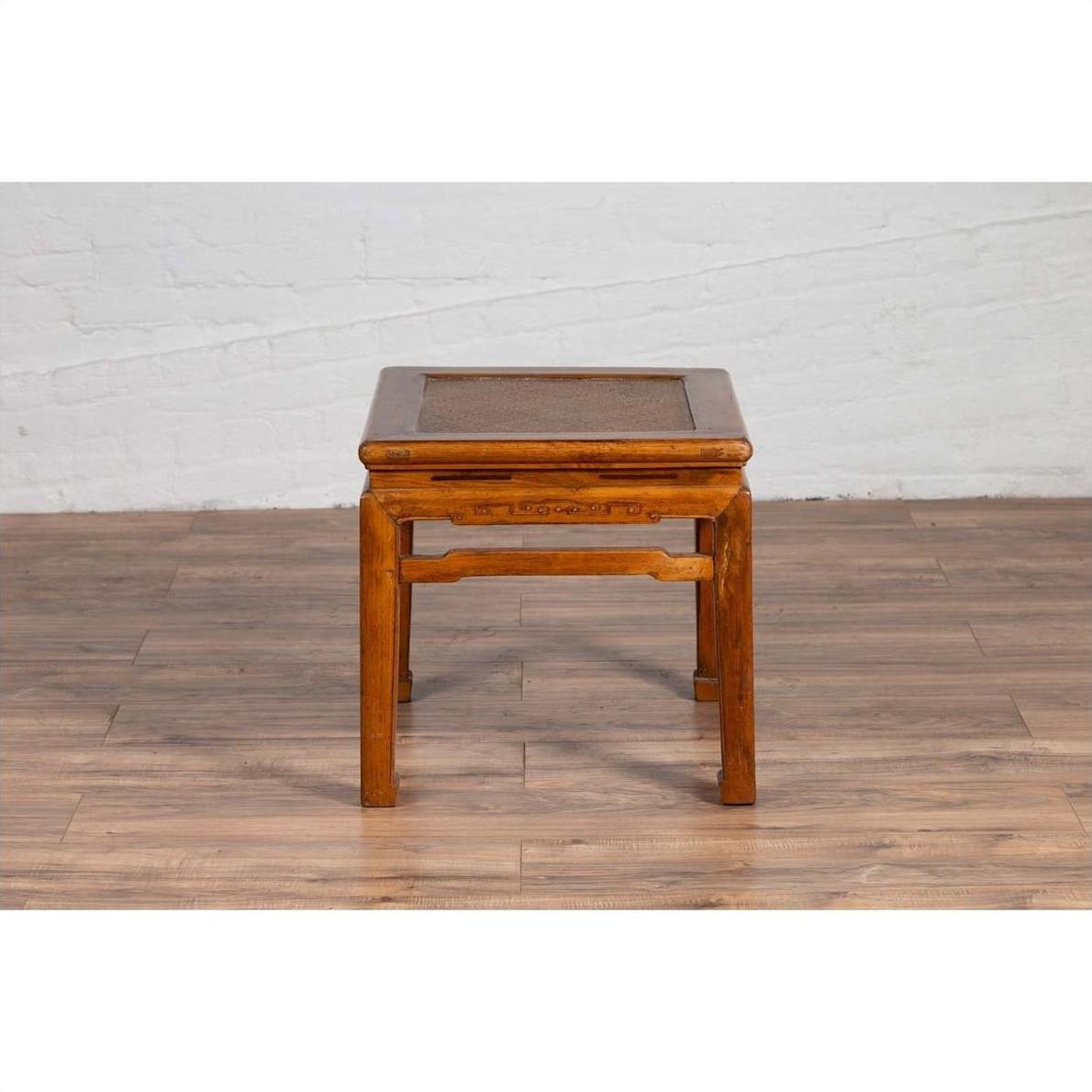 Brown elmwood Ming style side table with horsehoof legs on a wooden floor against a white brick wall.