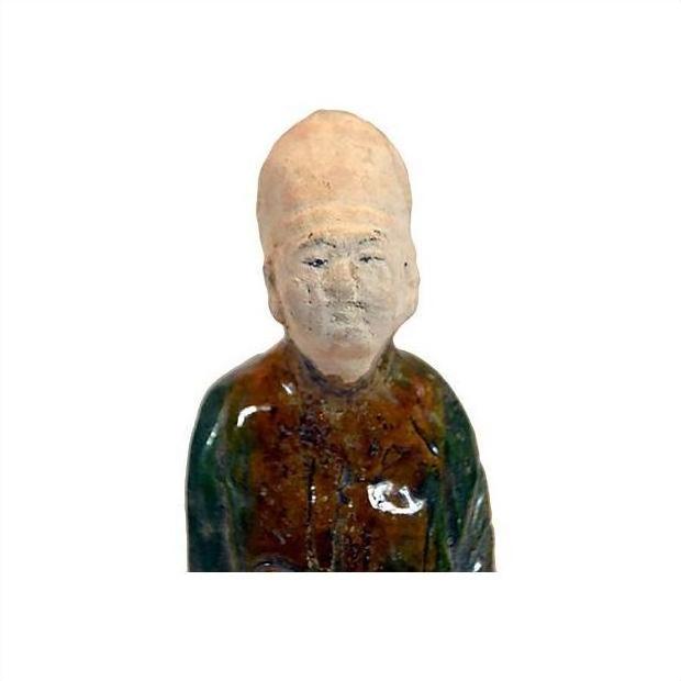 Green-brown terracotta court figure statue with tall hat, close-up on white background.